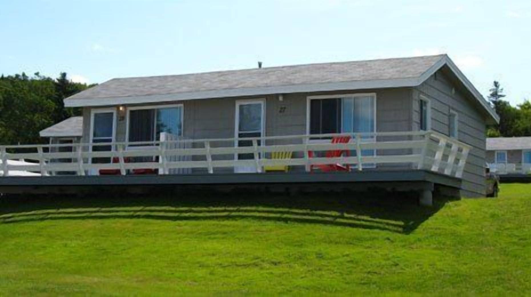 A single-story building with a flat roof, a covered porch with white railings, and a grassy lawn.