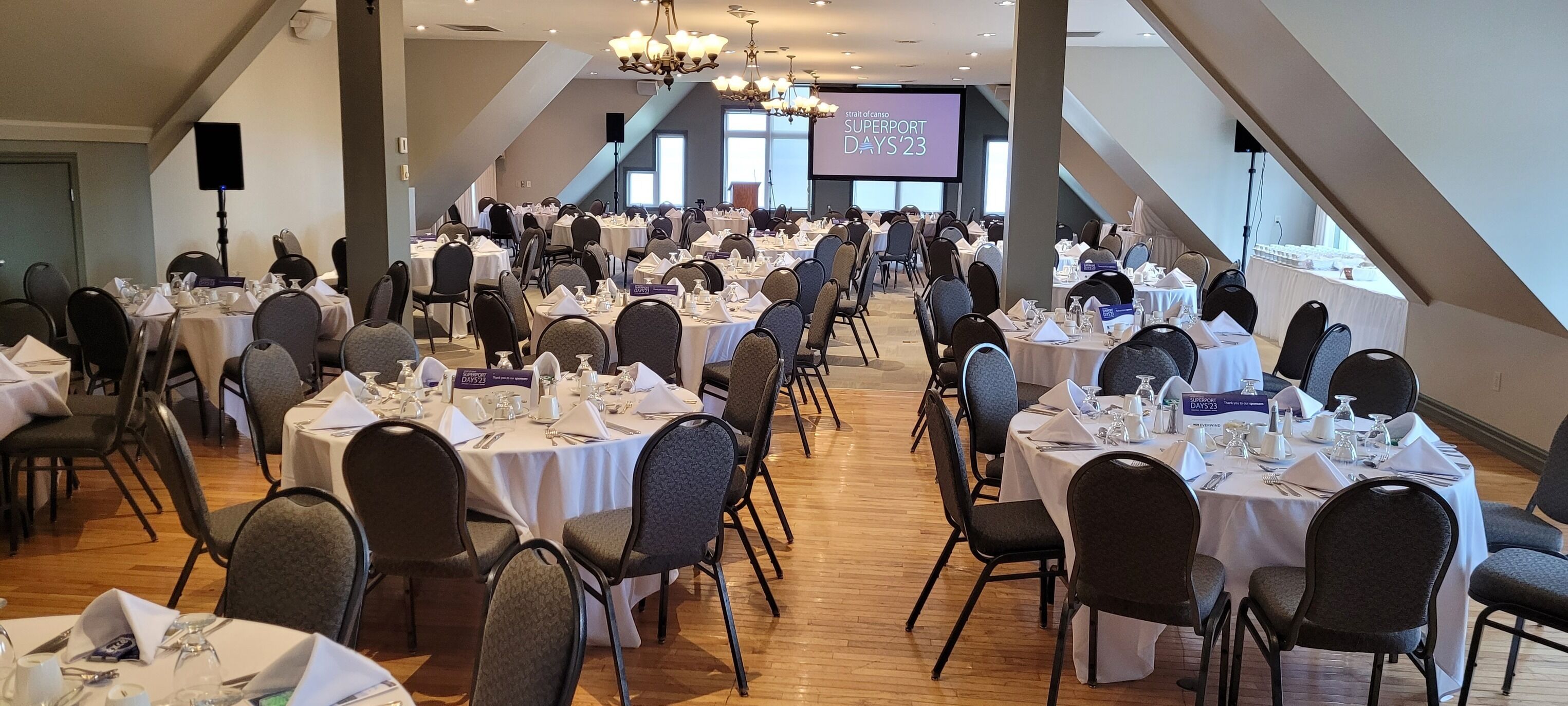 Un gran salón de banquetes con varias mesas redondas dispuestas para cenar, con tarjetas de nombres y vajilla.