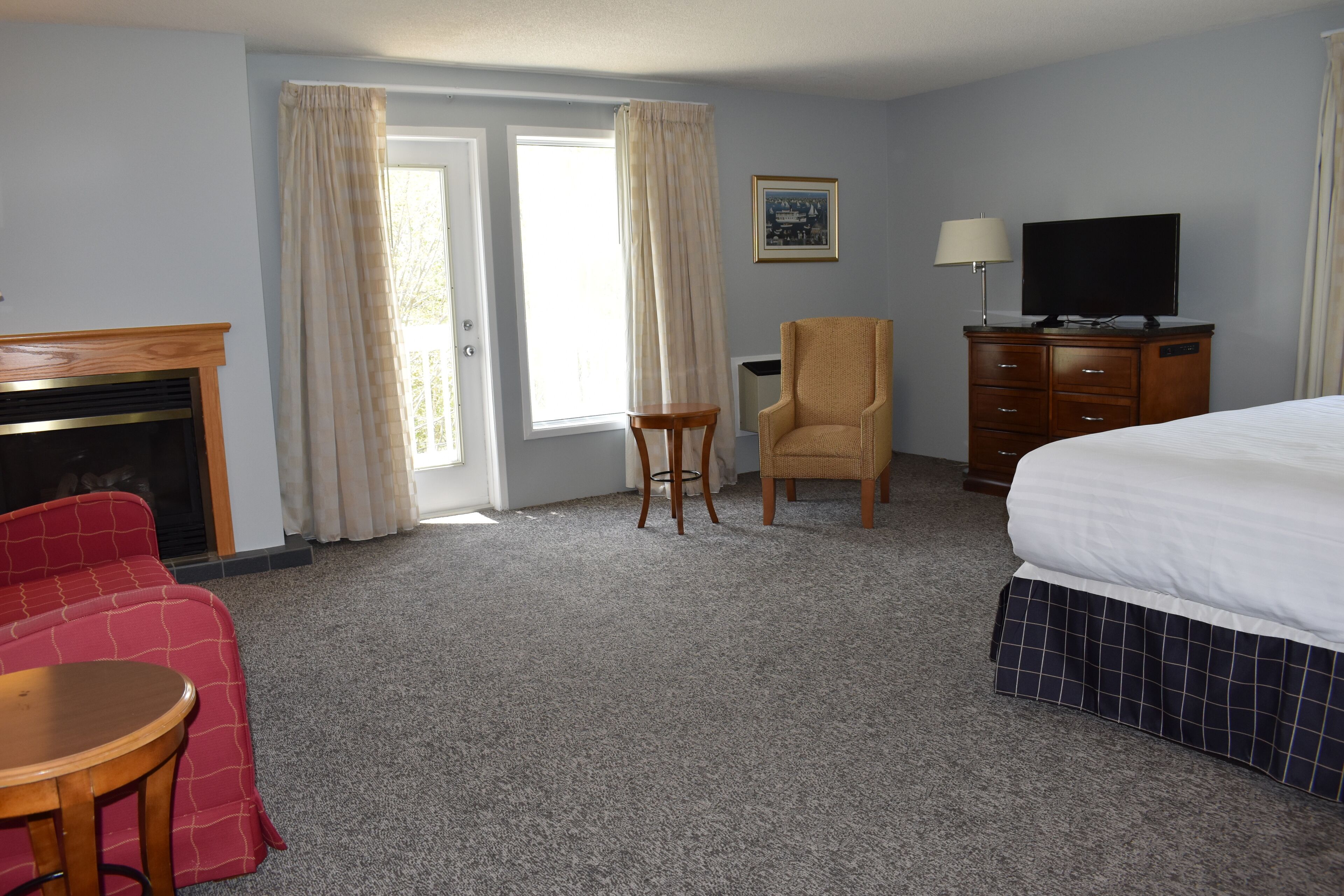 Habitación de hotel con cama, televisión, silla, mesita, cómoda y chimenea.