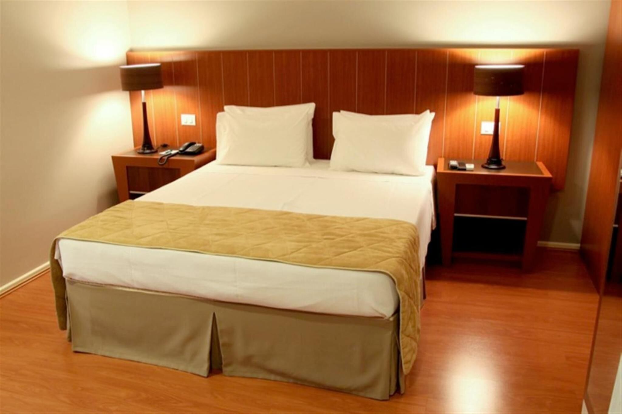 Una habitación de hotel con una cama grande, dos mesitas de noche con lámparas y un cabecero de madera.