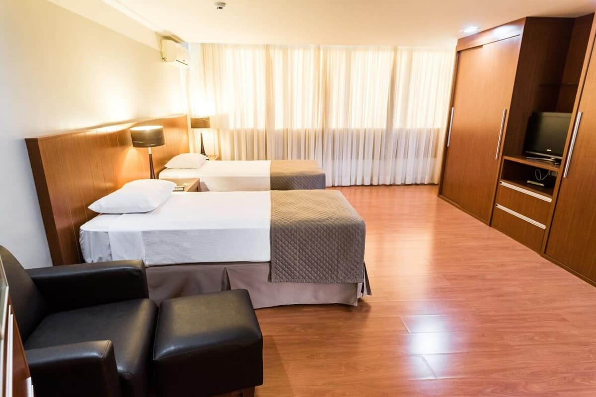 A hotel room with two beds, a TV, a wardrobe, and a seating area.