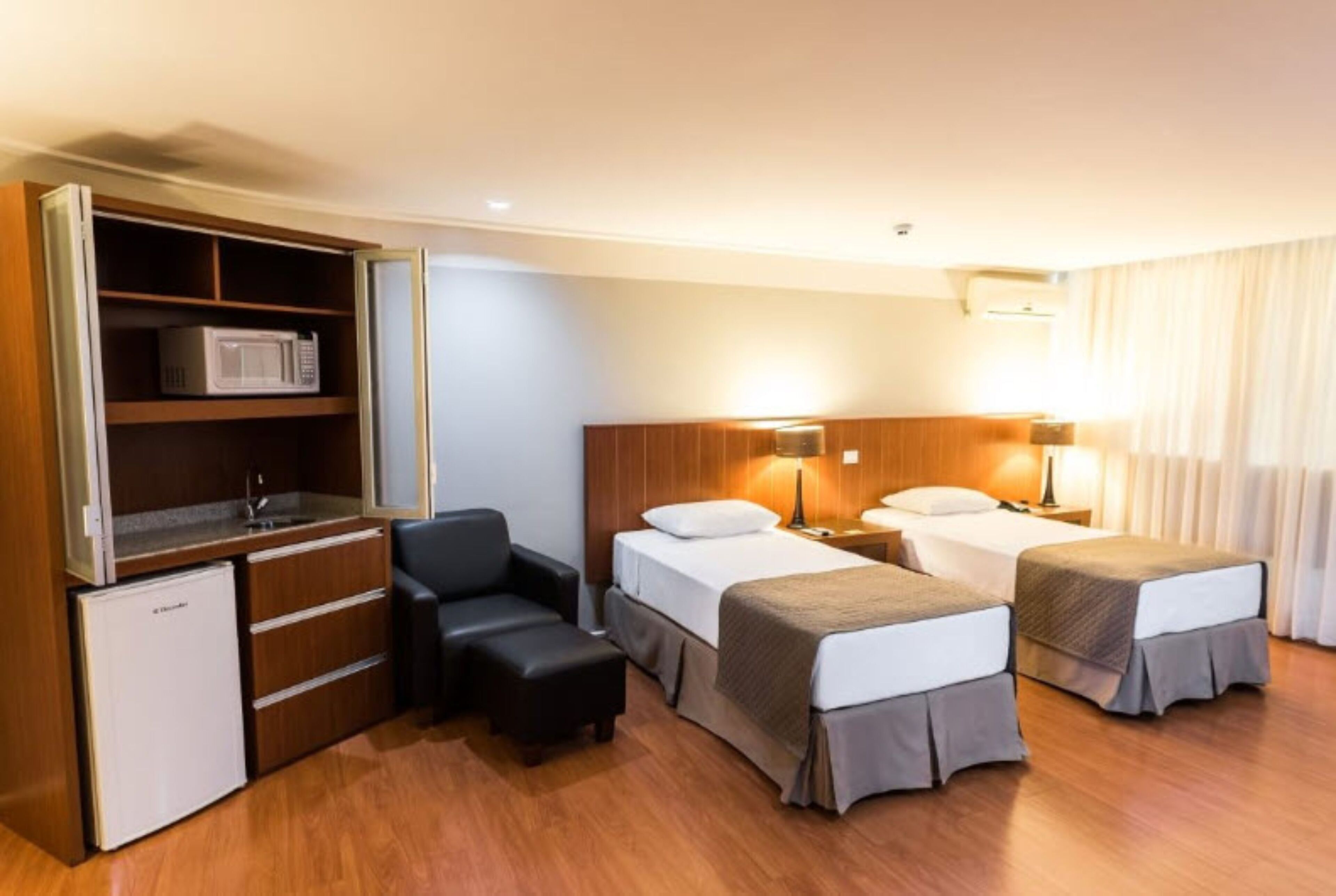 A hotel room with two beds, a desk with a microwave, a mini-fridge, and a seating area.