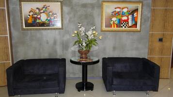 A lobby with two black armchairs, a glass table with a vase of white flowers, and two framed artworks on the wall.