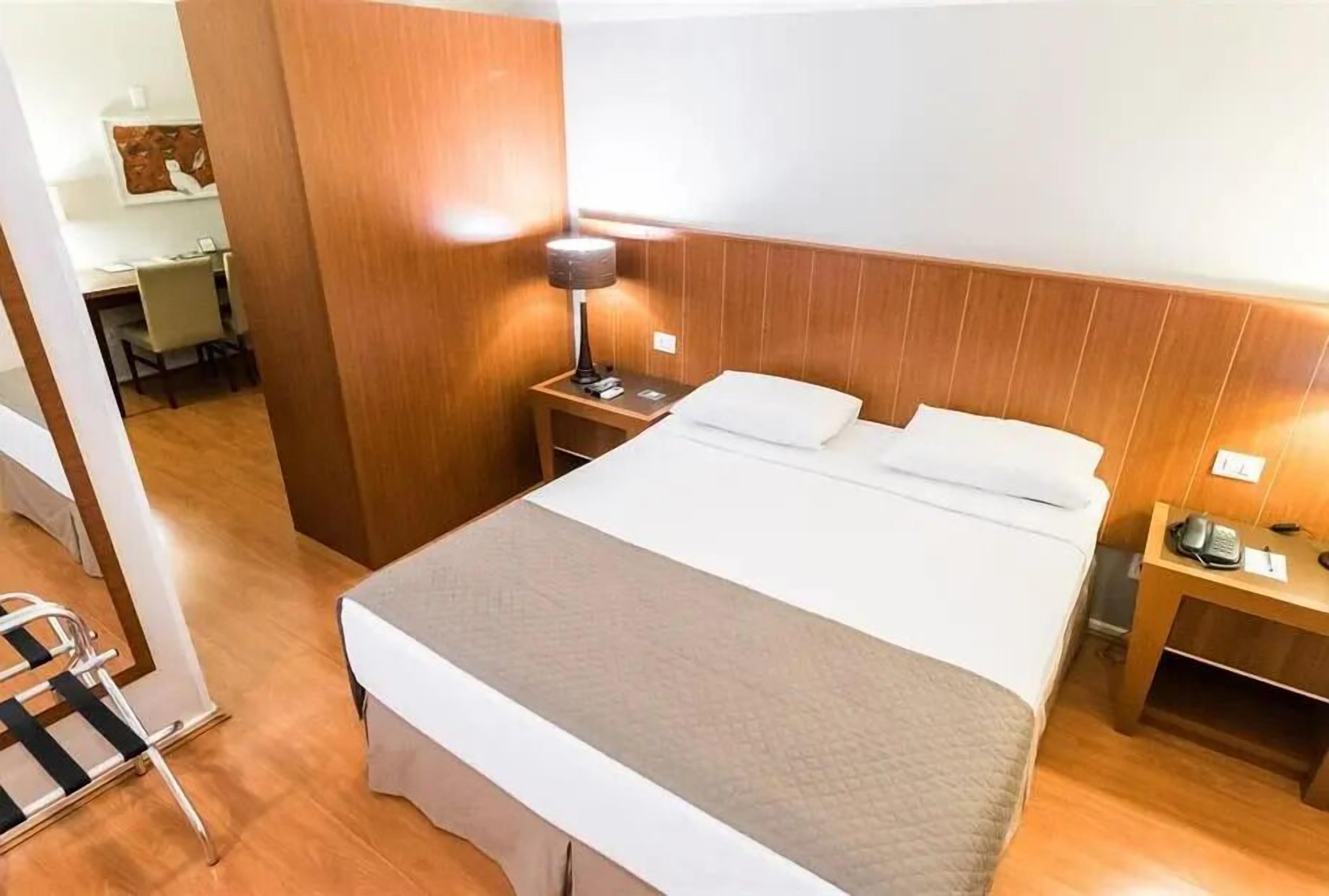 A hotel room with a bed, bedside table, lamp, and a desk with a chair.