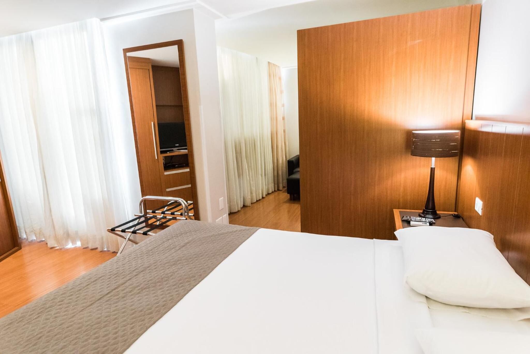 Habitación de hotel con cama, armario de madera, escritorio con lámpara y zona de estar con una silla y una mesa.