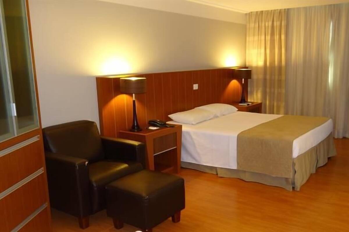 A hotel room with a bed, a chair, a desk, a lamp, and a television.