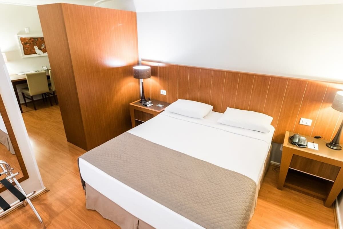 A hotel room with a large bed, wooden headboard, bedside tables with lamps, and a desk with a chair.