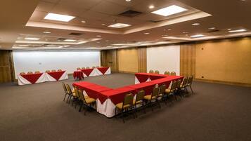 Un salón de conferencias con una larga mesa, sillas y una pantalla de proyector.