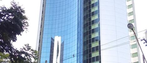 A modern high-rise building with a curved glass facade, surrounded by trees and a street.