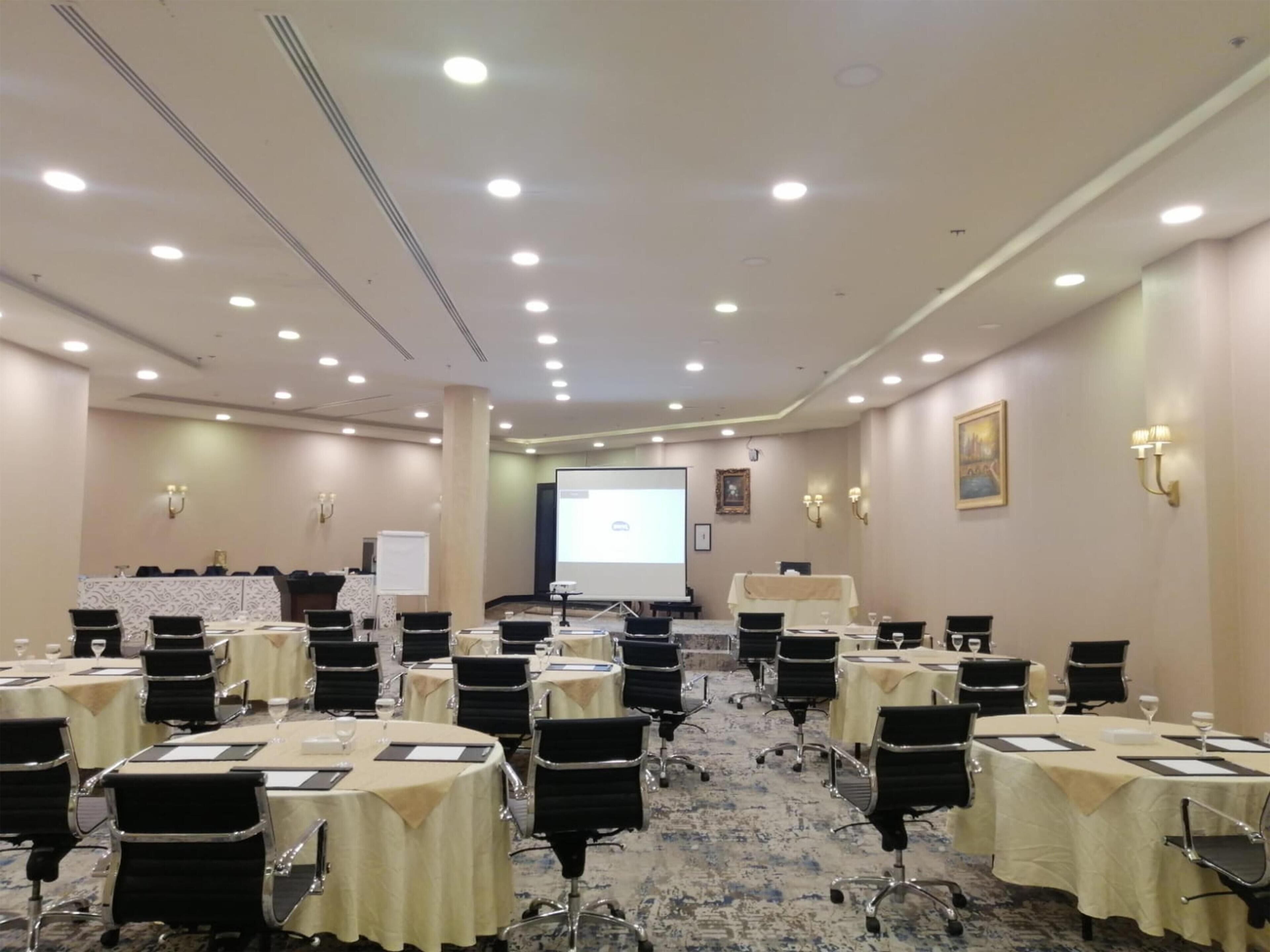 A conference room with multiple tables, chairs, a projector screen, and a whiteboard.