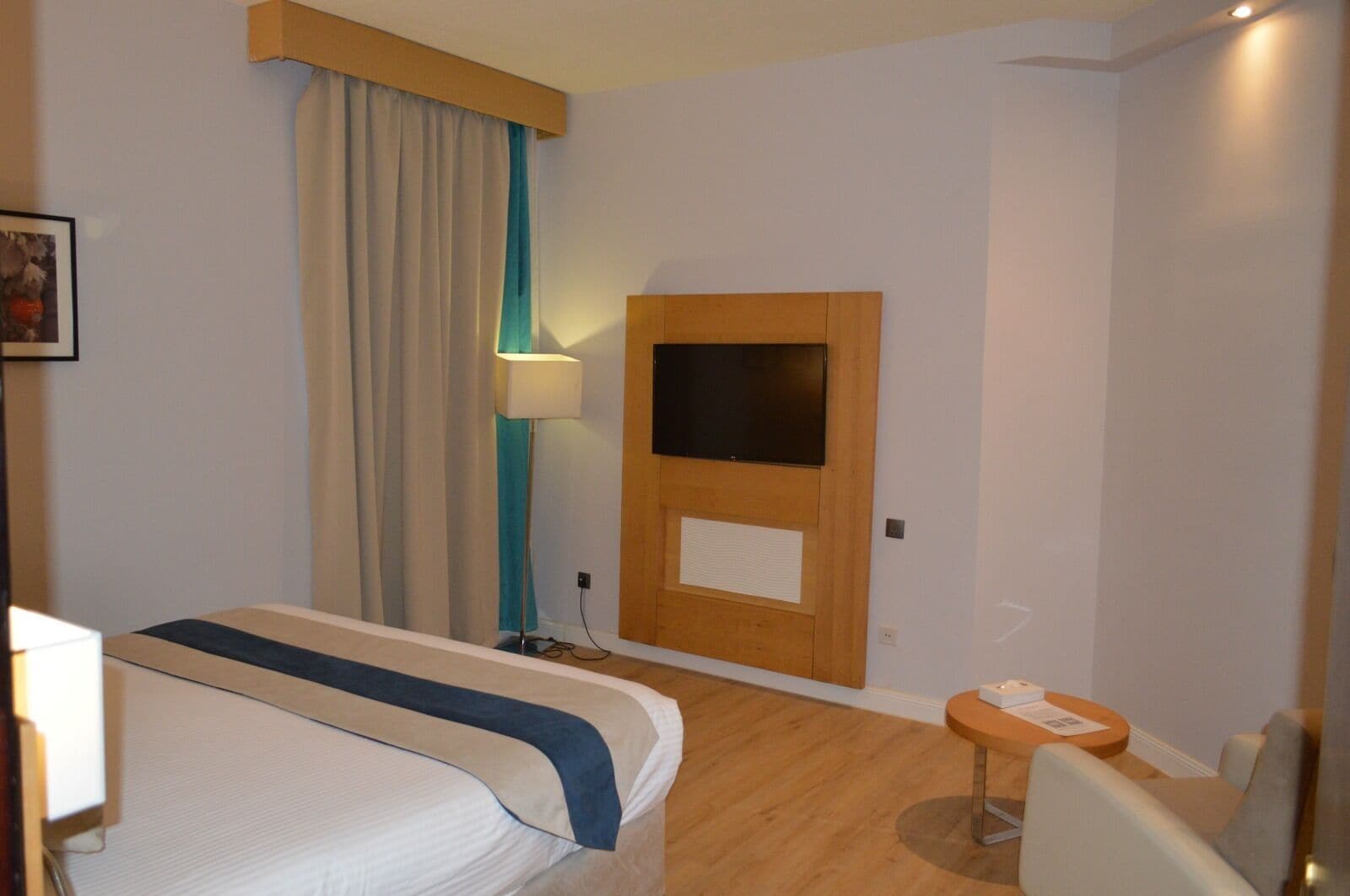 Habitación de hotel con cama, escritorio, silla, televisor y ventana con cortinas.