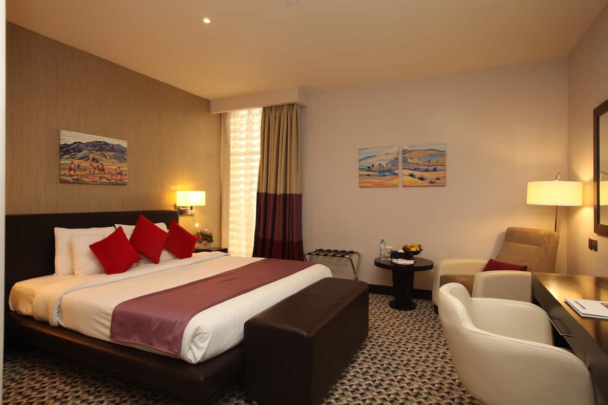 Quarto de hotel com uma cama grande, uma escrivaninha, uma cadeira e uma mesinha.