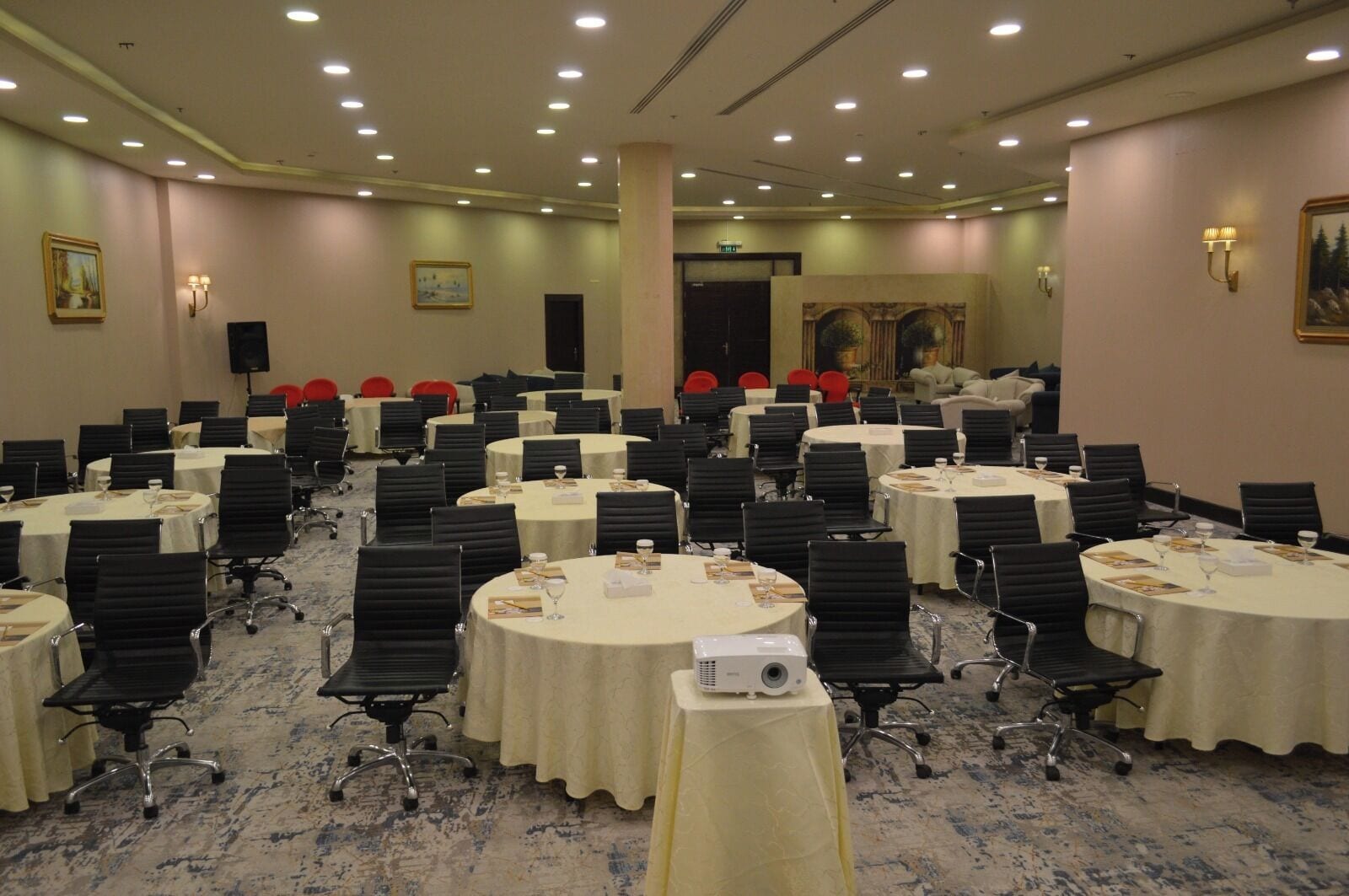 A conference room with multiple round tables, black chairs, and a carpeted floor.