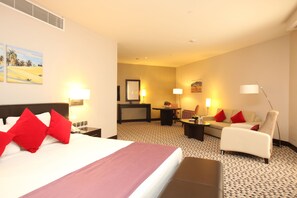 A hotel room with a large bed, a sofa, a desk, and a chair. There are paintings on the wall and a lamp on the desk. - Golden Tulip Hail (Ha'il)