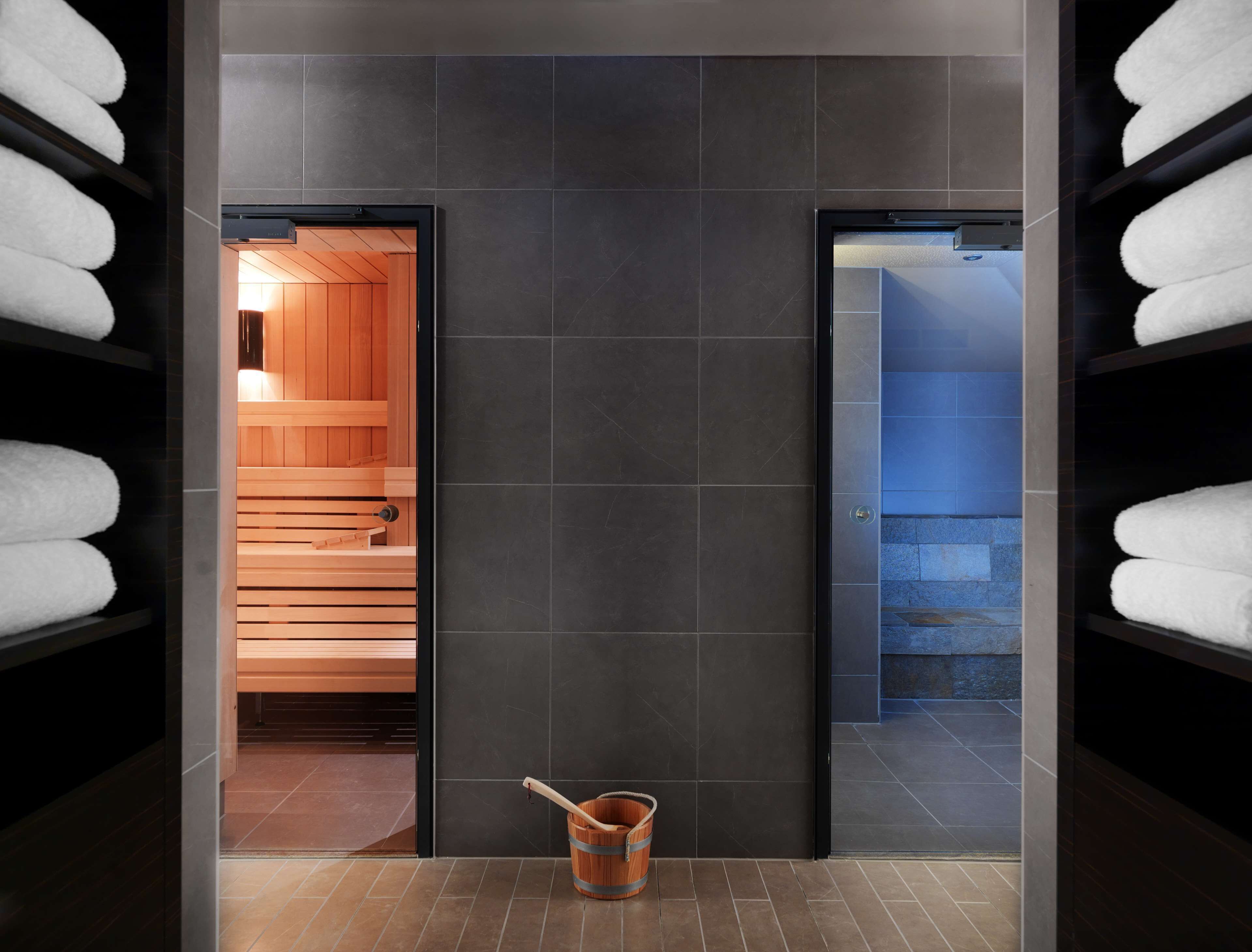 Een moderne badkamer met donkere betegelde wanden, houten bankjes en een houten emmer.
