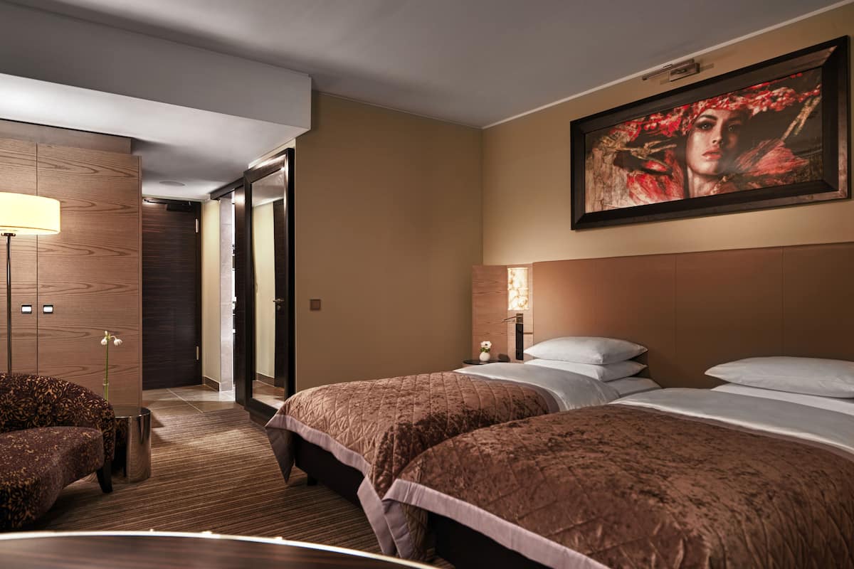 Hotellihuone, jossa on kaksi sänkyä, suuri taulu seinällä, työpöytä ja tuoli.