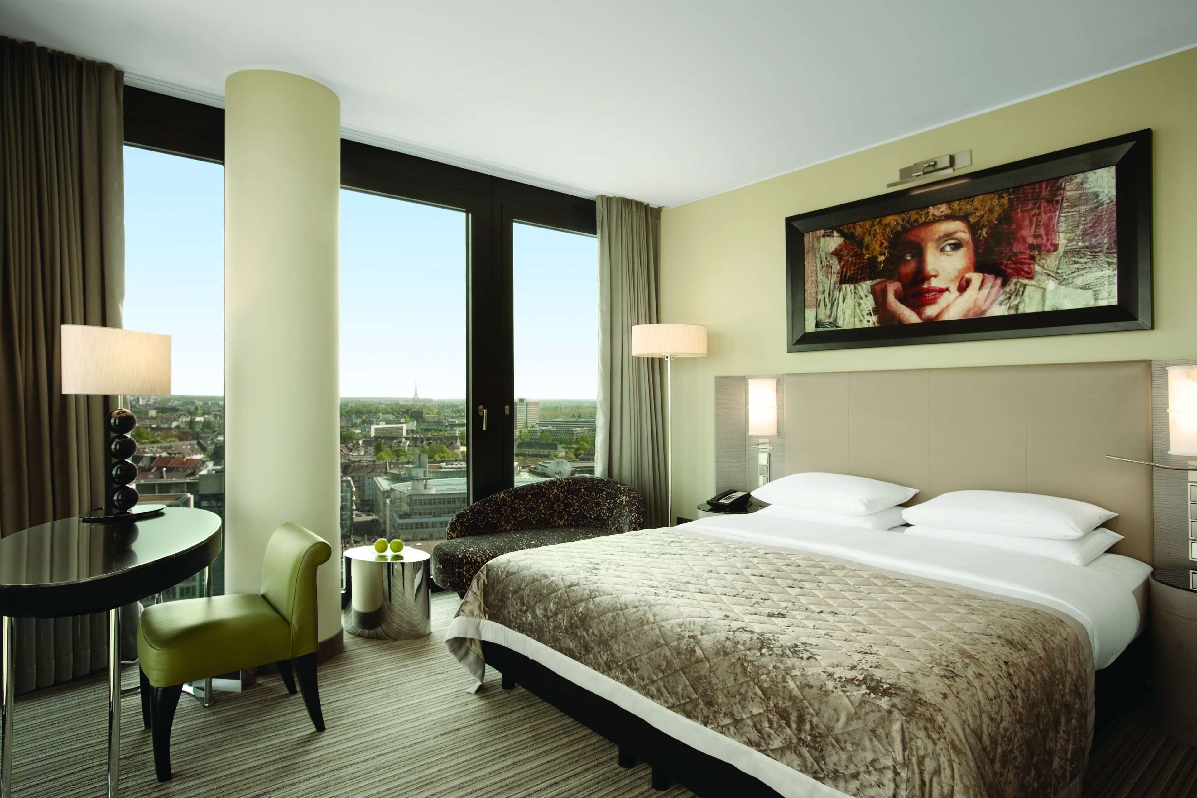 Habitación de hotel con una cama grande, un escritorio, una silla y vista a la ciudad.