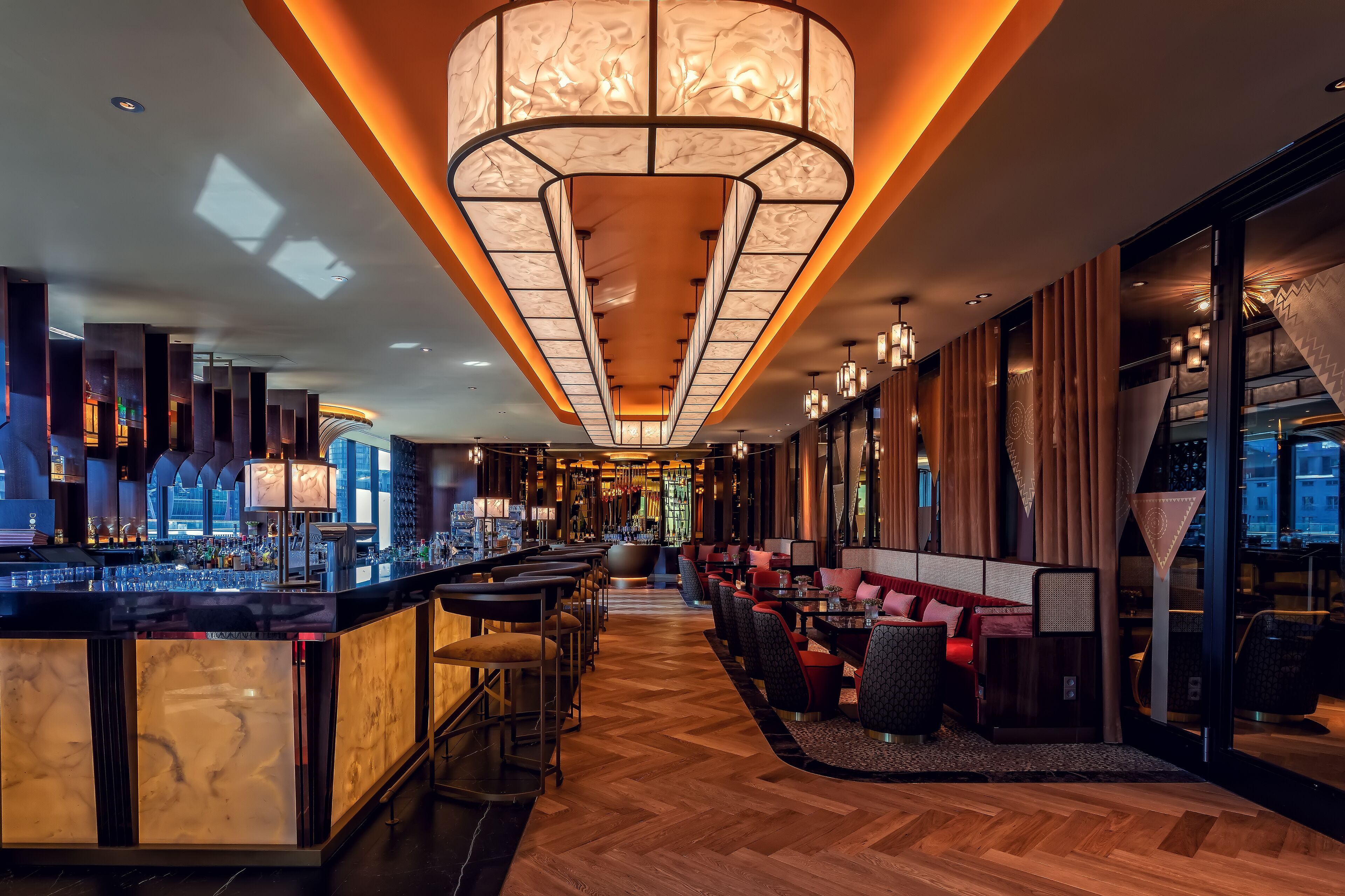 Un área de bar moderna con una barra larga, asientos y una luminaria amplia e iluminada en el techo.