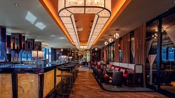 Un área de bar moderna con una barra larga, asientos y una luminaria amplia e iluminada en el techo.