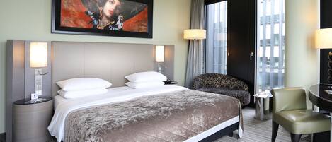 Una habitación de hotel con una cama grande, dos mesitas de noche con lámparas, una silla y un cuadro en la pared.