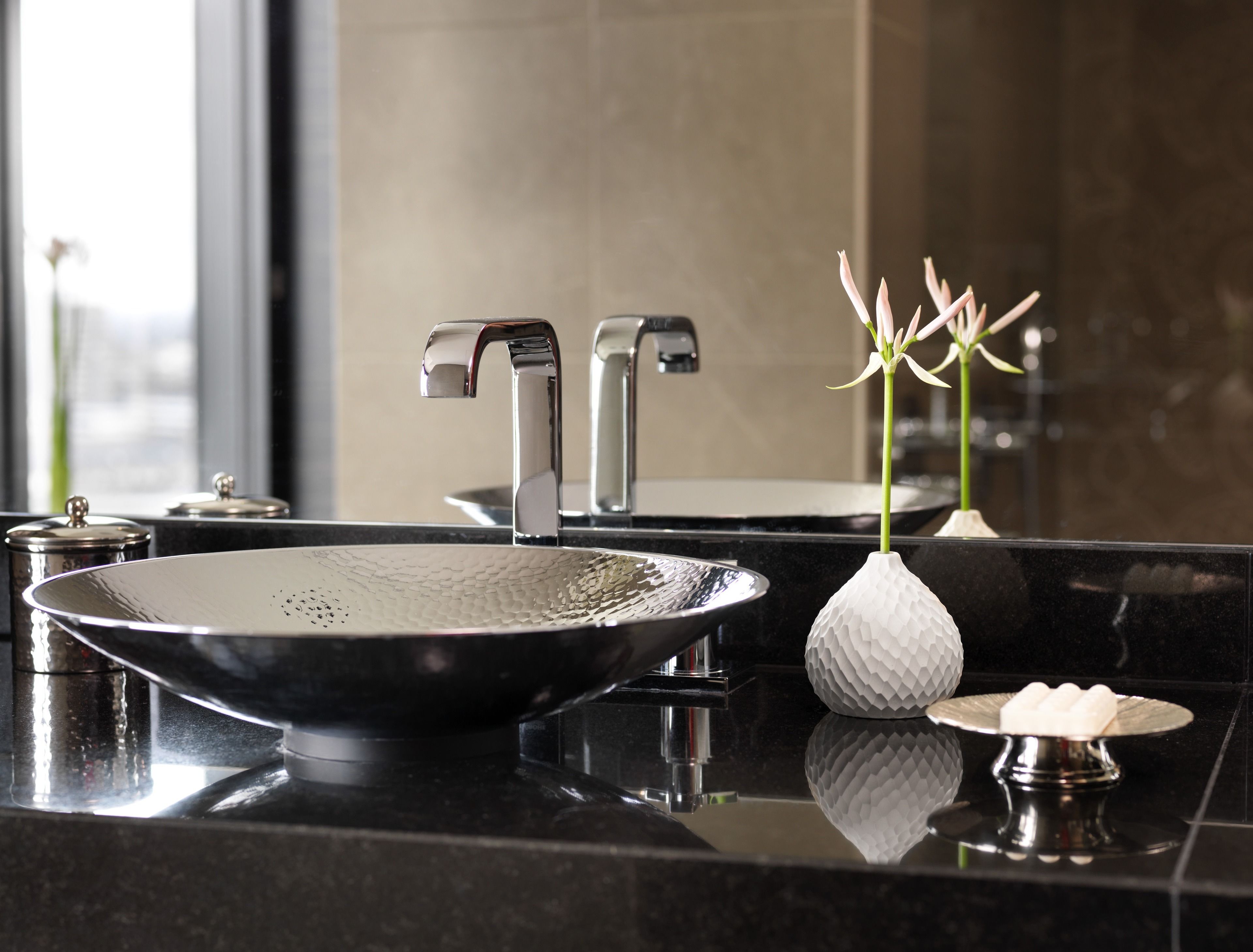 A modern bathroom with a large, round, textured sink and two chrome faucets.
