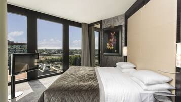 Ein Hotelzimmer mit einem großen Bett, einem Fernseher und Blick auf die Stadt durch große Fenster.