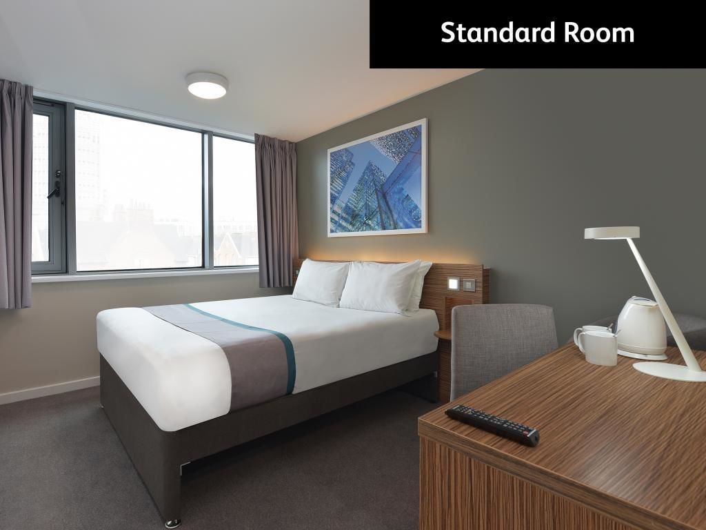 A standard room with a bed, a desk, a chair, a lamp, and a window with curtains.