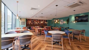 A modern restaurant interior with wooden flooring, various seating arrangements, and a large window providing natural light. - Travelodge London Central Waterloo (London)