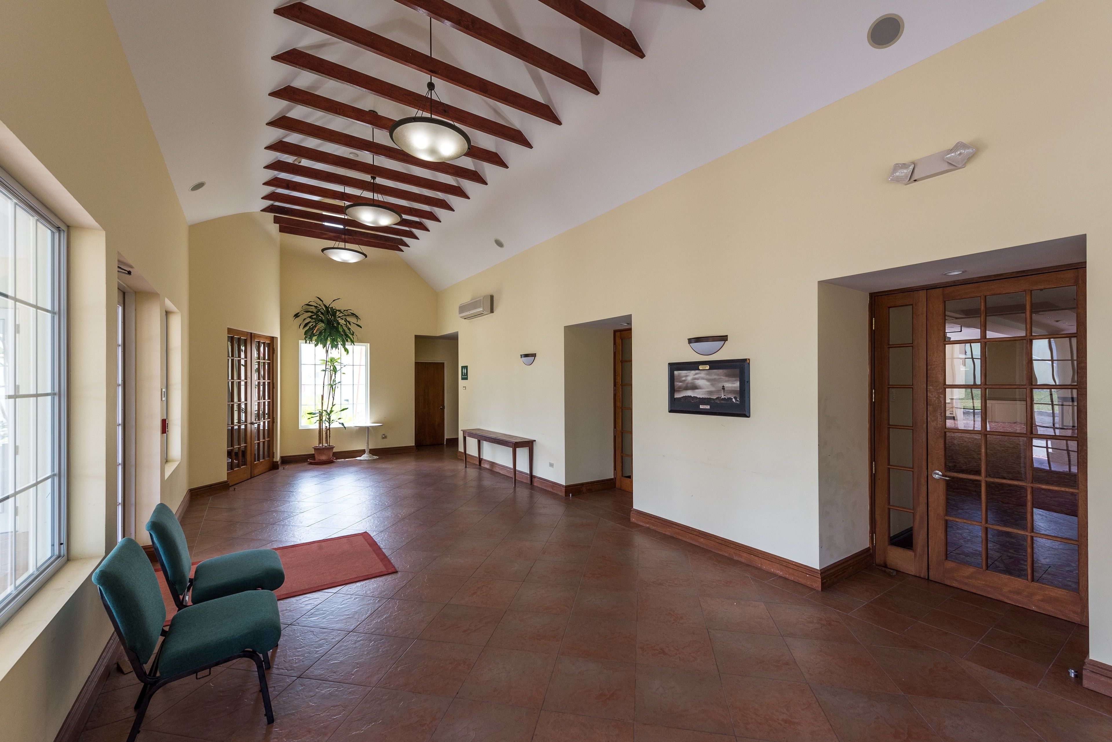 A spacious hallway with wooden beams on the ceiling, a potted plant, a bench, and a door with glass panels.