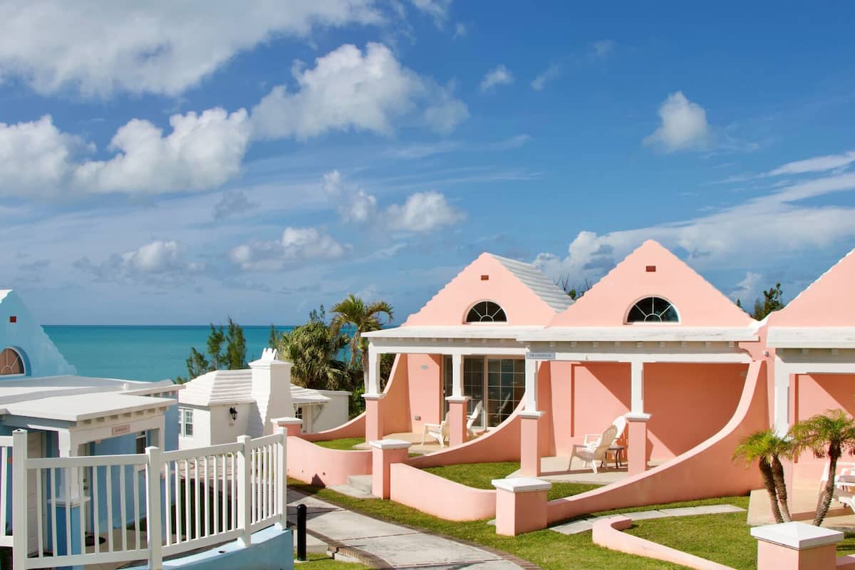 Um resort com edifícios cor-de-rosa e brancos, área de piscina e vista para o oceano.