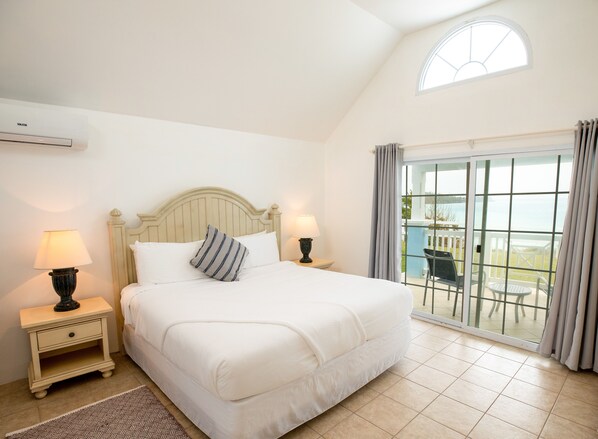 A bedroom with a bed, two bedside tables with lamps, a window with curtains, and a view of the outdoors.