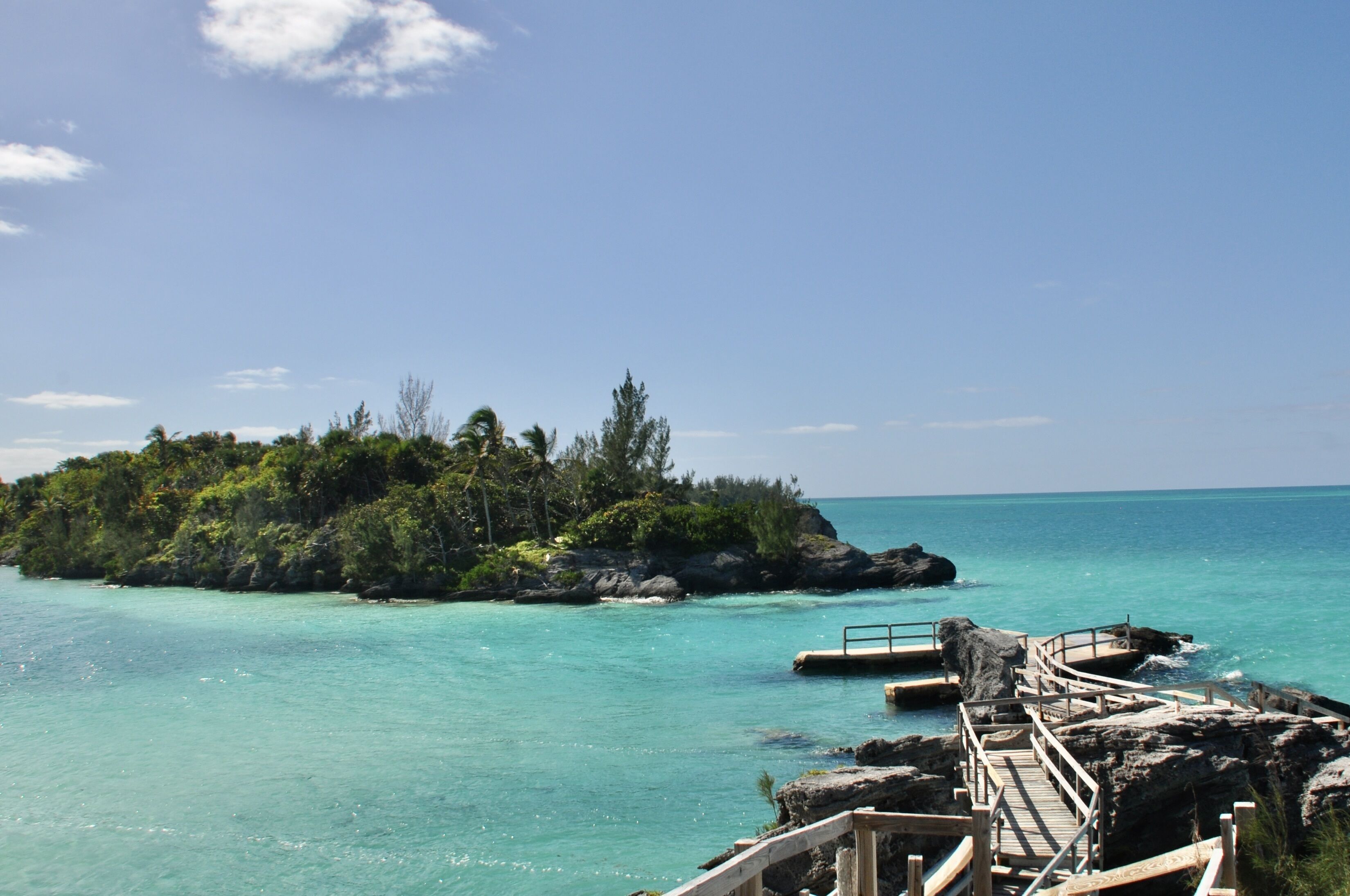 Un muelle de madera que conduce a una pequeña isla con abundante vegetación y aguas turquesas cristalinas.