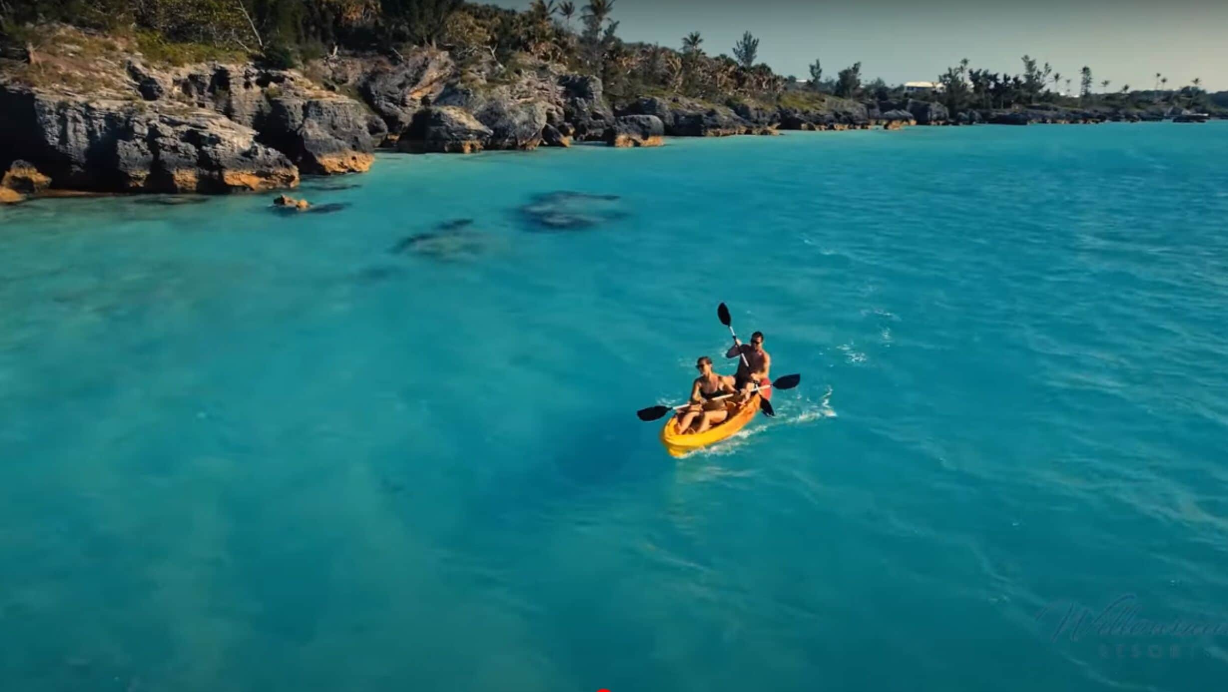Un kayak su acque cristalline turchesi, con una costa rocciosa e palme sullo sfondo.