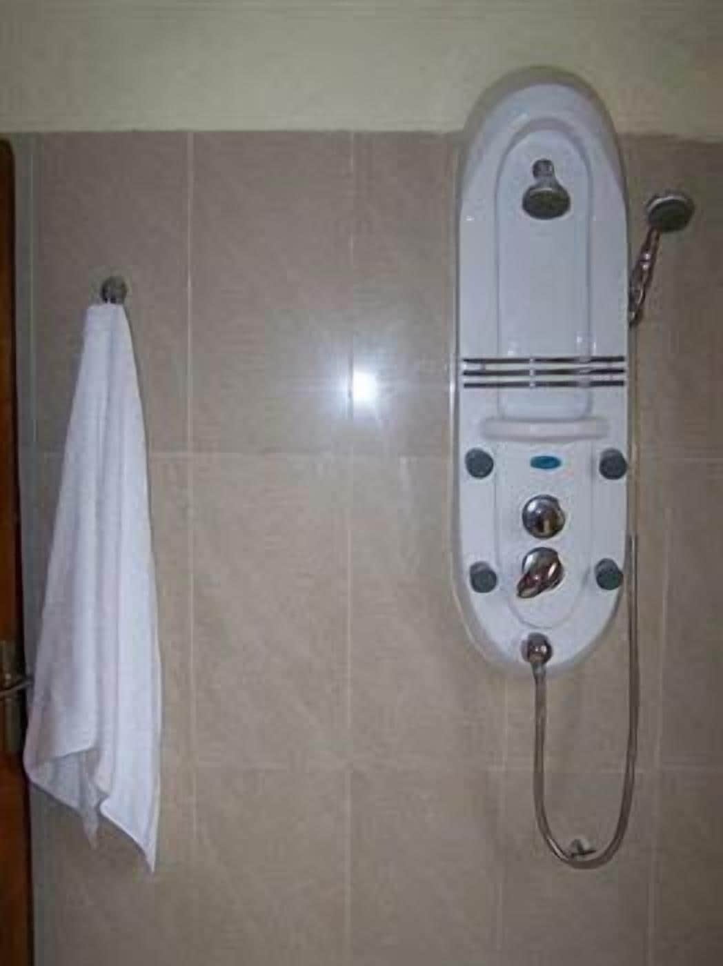 A bathroom with a shower, a towel hanging on a rack, and a tiled wall.
