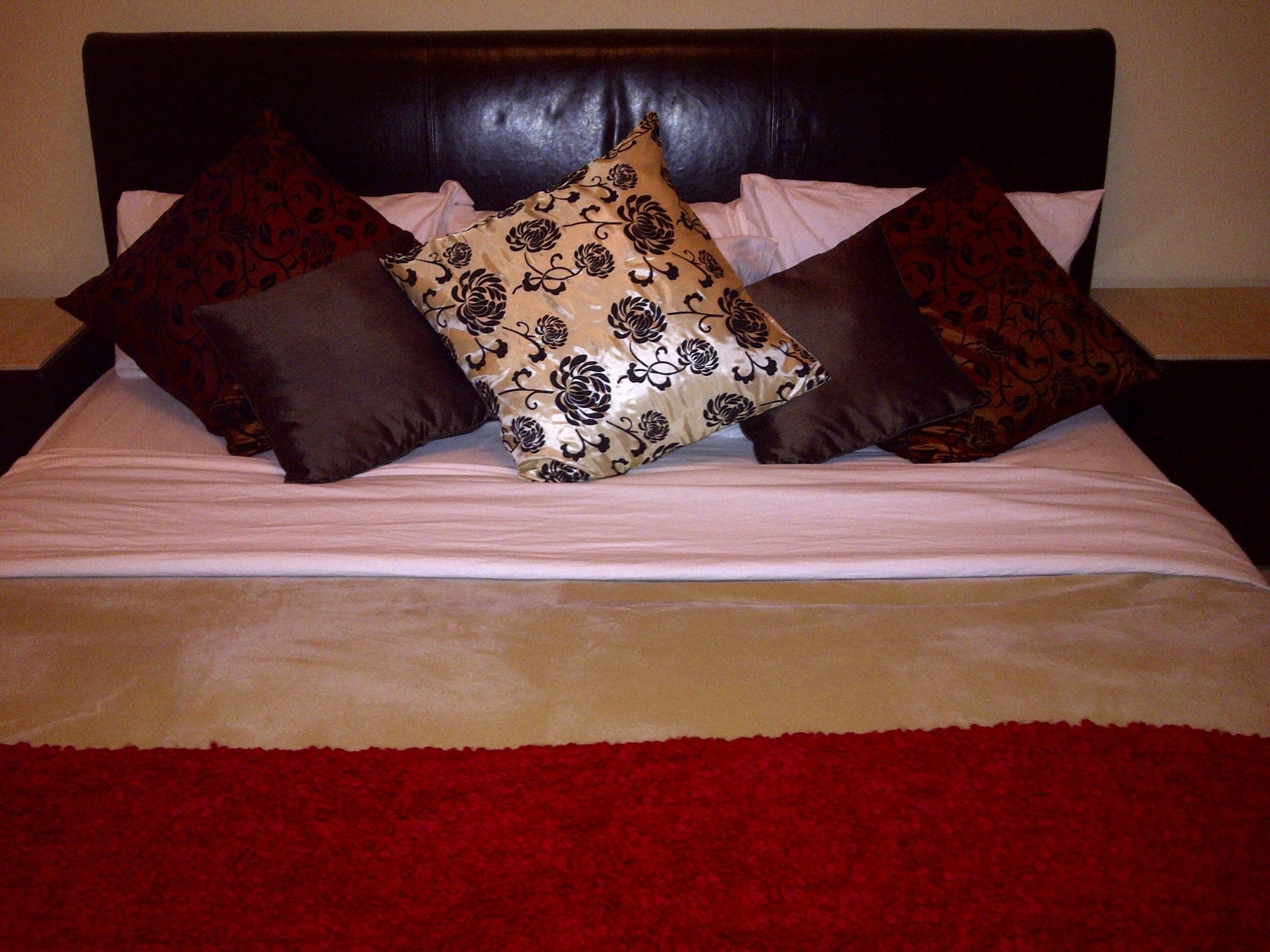 A bed with a dark headboard, multiple pillows, and a red and beige bedspread.
