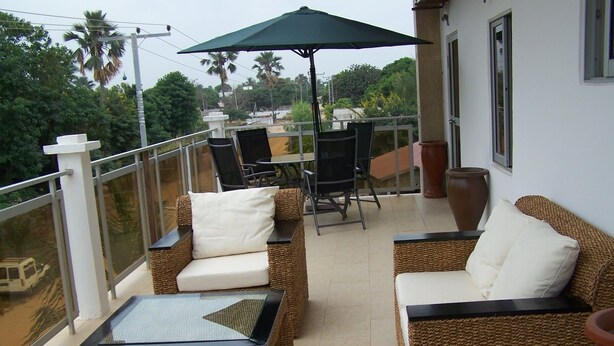 Een balkon met rieten meubels, een glazen tafel en een grote parasol.