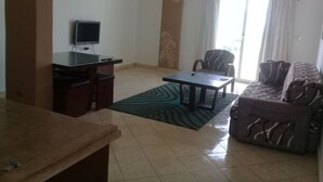 A living room with a TV, a sofa, a patterned rug, and a window with curtains. - Carlton Luxury Resort (Sharm El Sheikh)