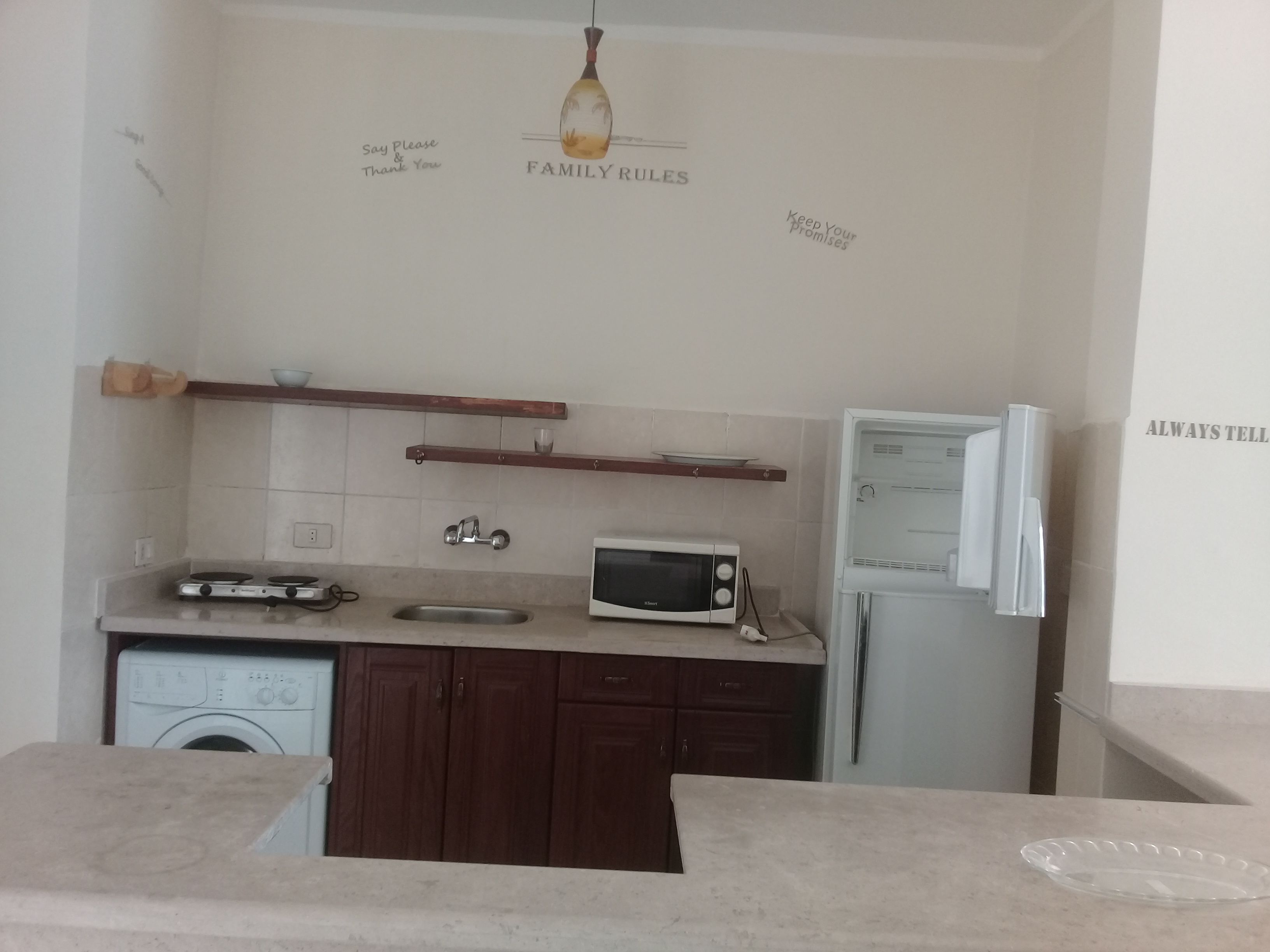 A small kitchen with a washing machine, a microwave, a sink, and a refrigerator.