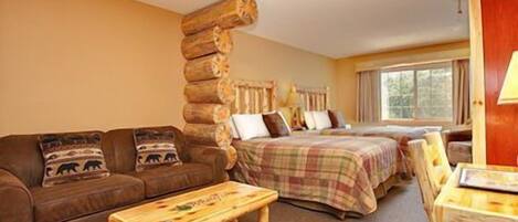Ein gemütliches Zimmer mit einer großen Holzwand, einer Couch mit Tierkissen, einem Bett mit kariertem Überwurf und einem kleinen Holztisch.