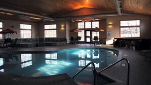 An indoor swimming pool with stone walls, wooden ceiling, and large windows. - Whitefish Lodge and Suites (Crosslake)