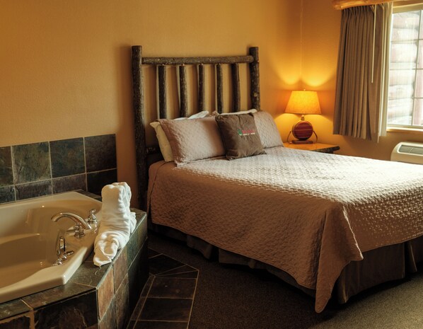 A hotel room with a bed, a nightstand, a lamp, a bathroom with a bathtub, and a window with curtains.