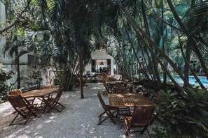 Un jardín tropical interior con mesas y sillas de madera, una piscina y abundante follaje.