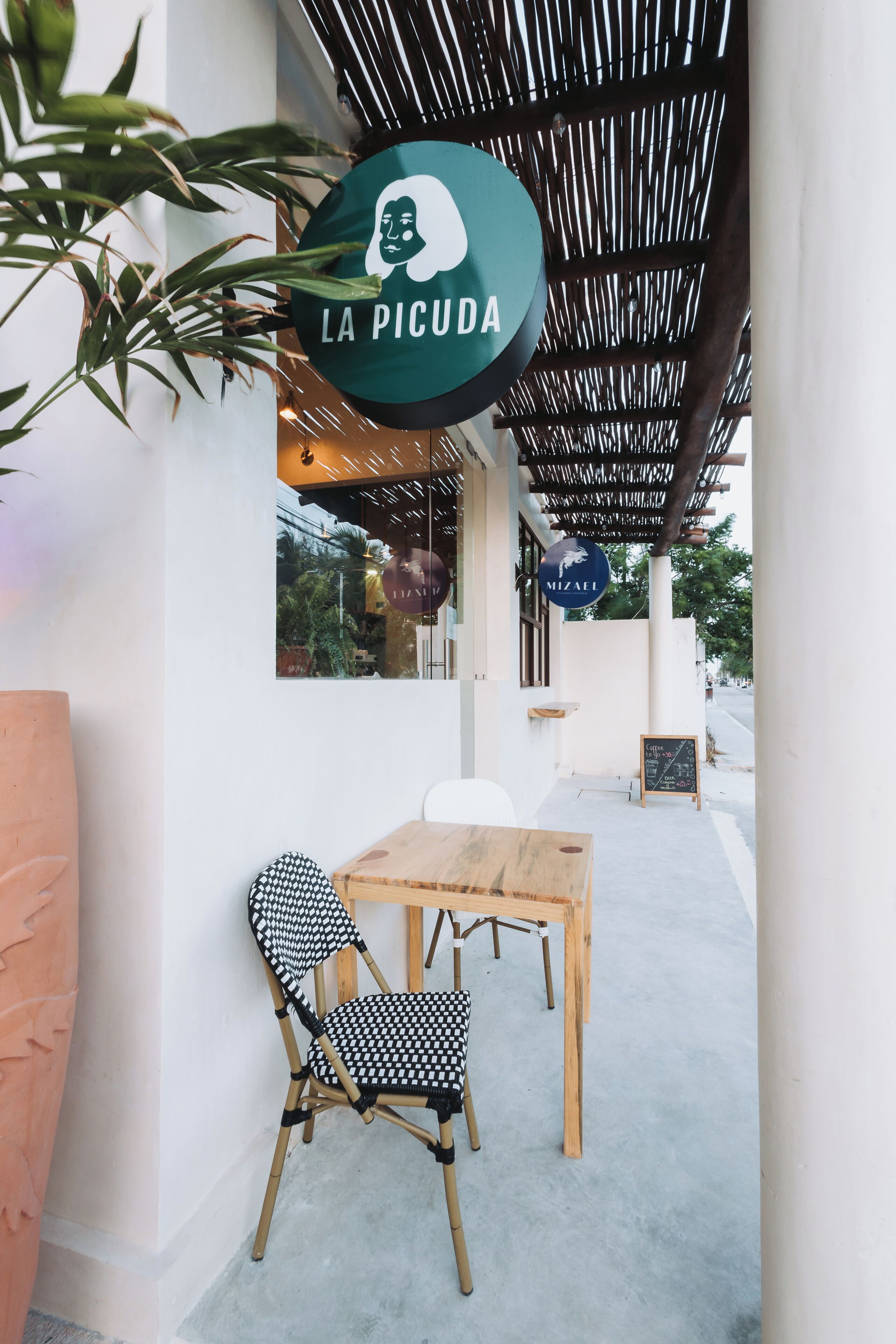 An outdoor seating area with a wooden table and a black and white checkered chair. A sign with the text "LA PICUDA" is visible.