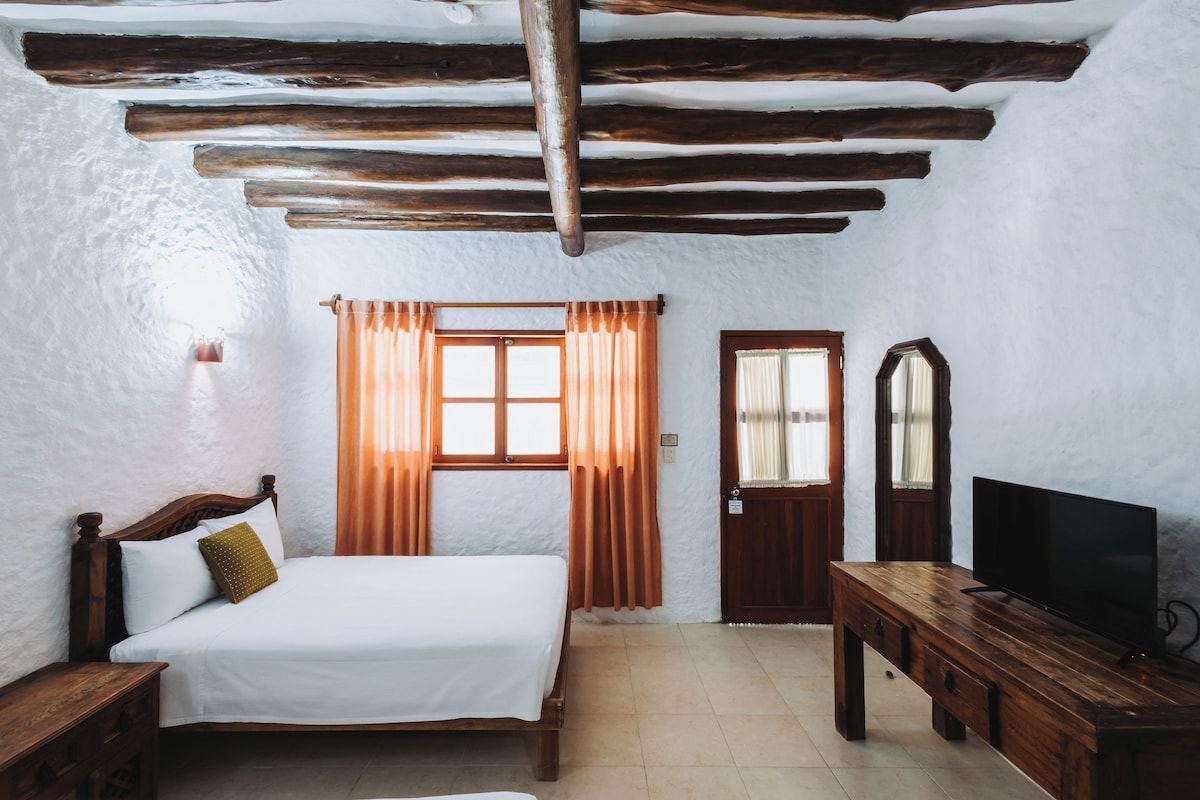 A room with a bed, a wooden desk, a television, and a door.