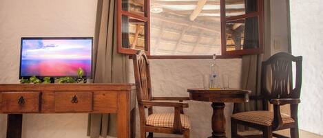 Un bureau en bois, une télévision, deux chaises et une fenêtre avec un cadre en bois.