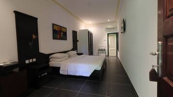 A hotel room with a bed, bedside table, wardrobe, and a painting on the wall.