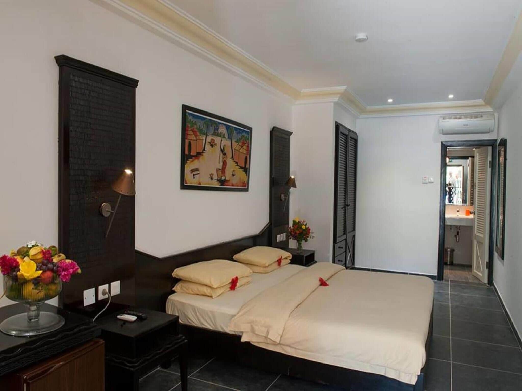 A hotel room with a bed, bedside tables, a painting, a lamp, and a flower vase.