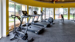 Een sportschool met meerdere loopbanden, hometrainers en een bank.