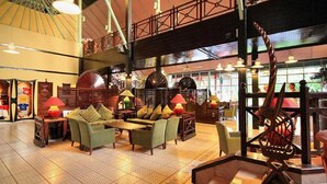 Een ruime lobby met een hoge plafond, grote ramen en een centraal gelegen zithoek met banken en stoelen.