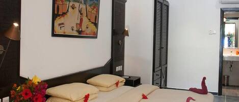 A hotel room with a bed, a nightstand, a lamp, a painting, and a bathroom visible through an open door.